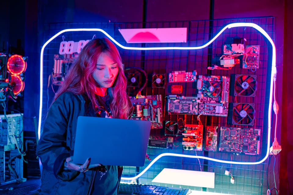 Asiatische Frau mit Laptop, in einem neonbeleuchteten Hackerspace